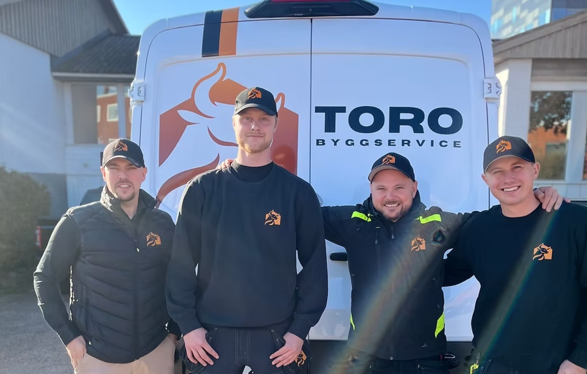 fyra personer i arbetskläder framför en bil med logotyp